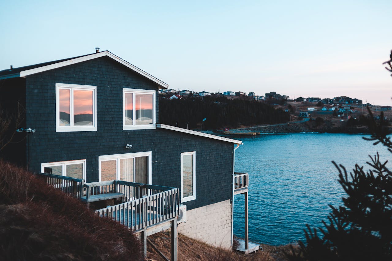 Brick building with fenced terrace and windows reflecting sky on mountain near growing trees and rippled ocean at sundown